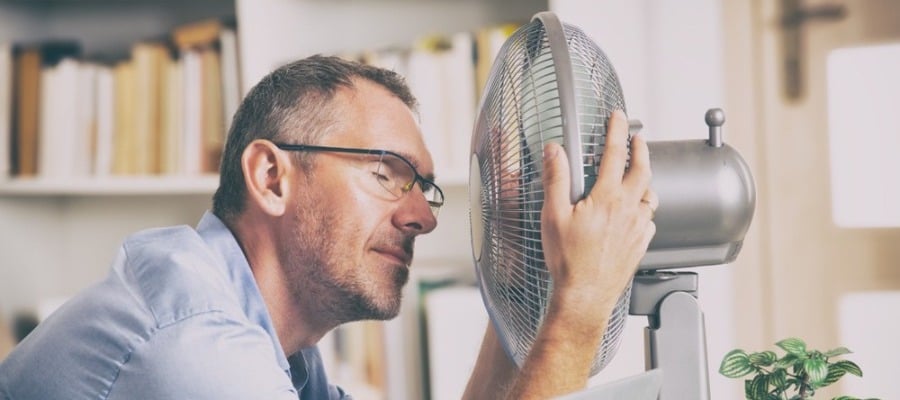 Image of man holding fan close to his face. 
