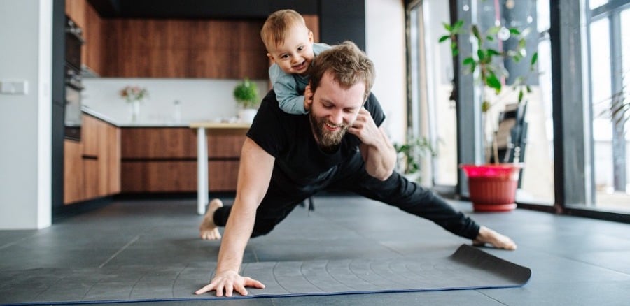 Father doing one-handed pushup with toddler on his back.