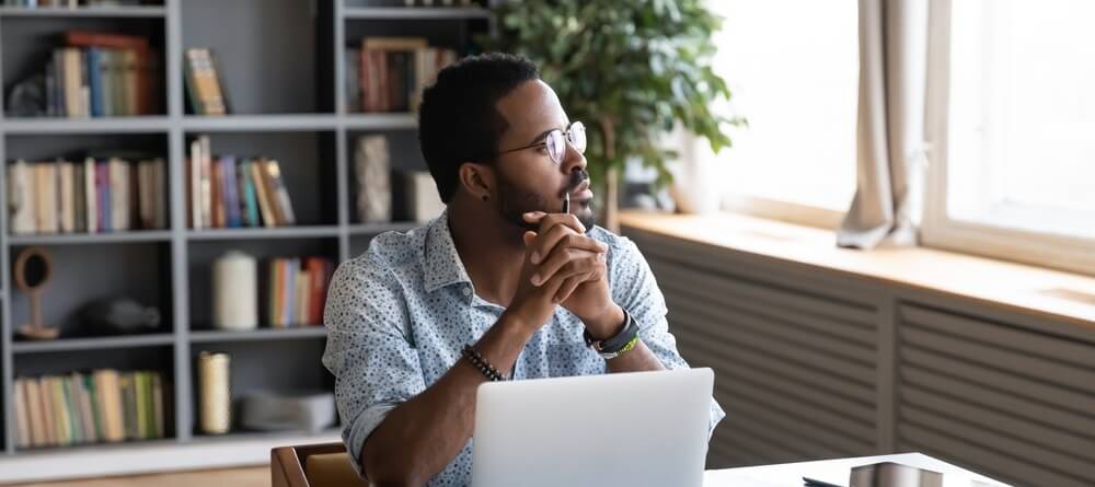 A man staring off into the distance to rest his eyes while working at his computer.