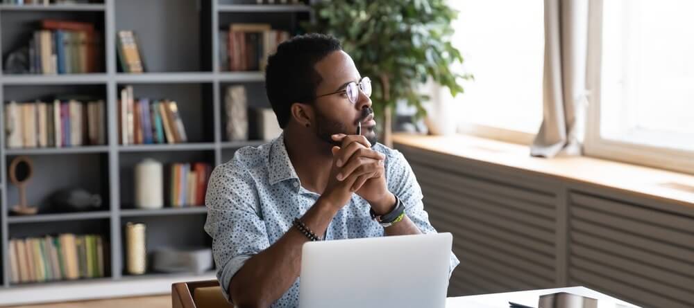 A man staring off into the distance to rest his eyes while working at his computer. 