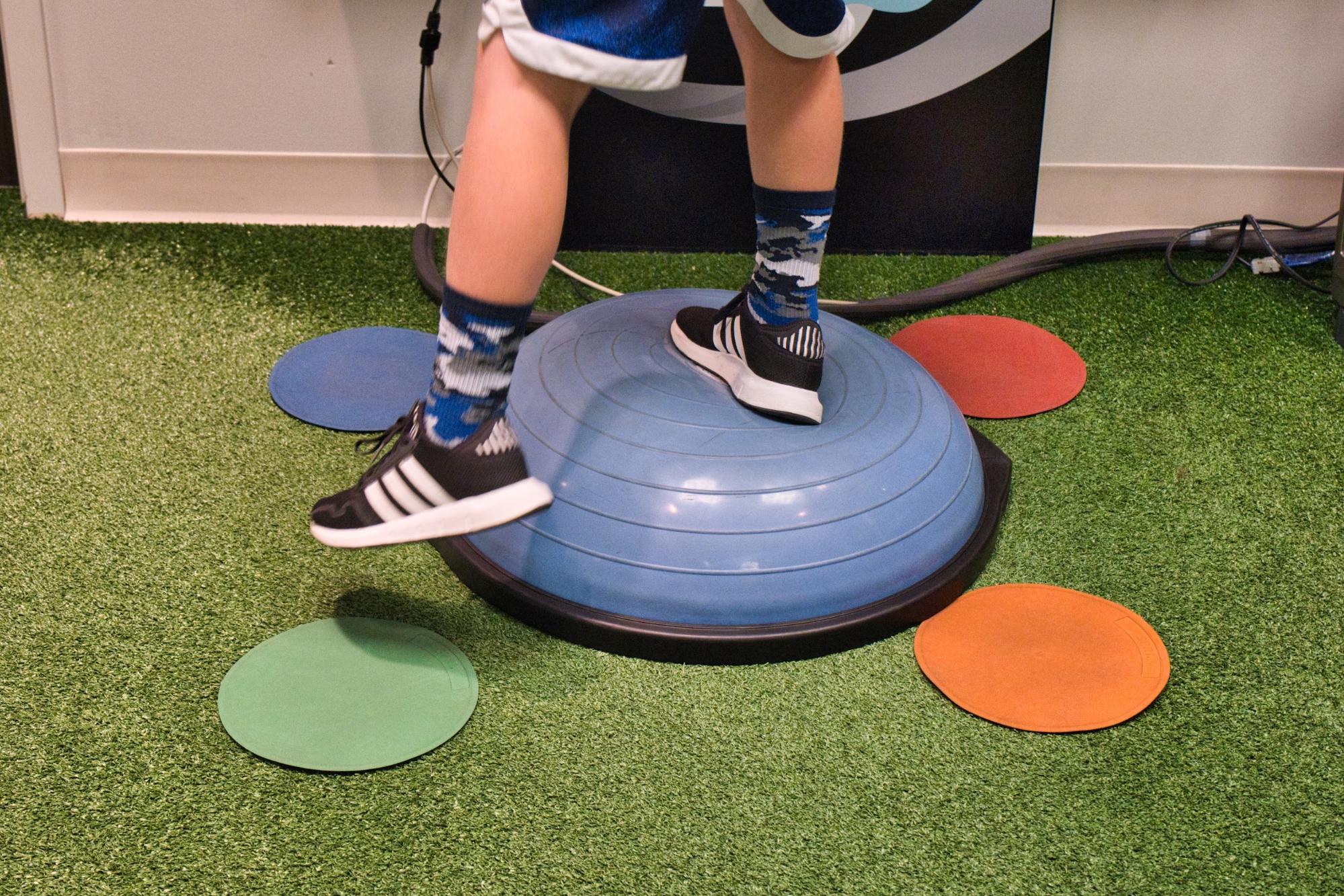 A young man balances on one foot on a bosu ball. 