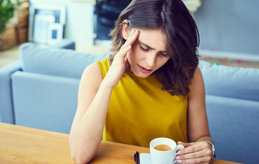 Woman grabs her head while sitting down at a table with an espresso