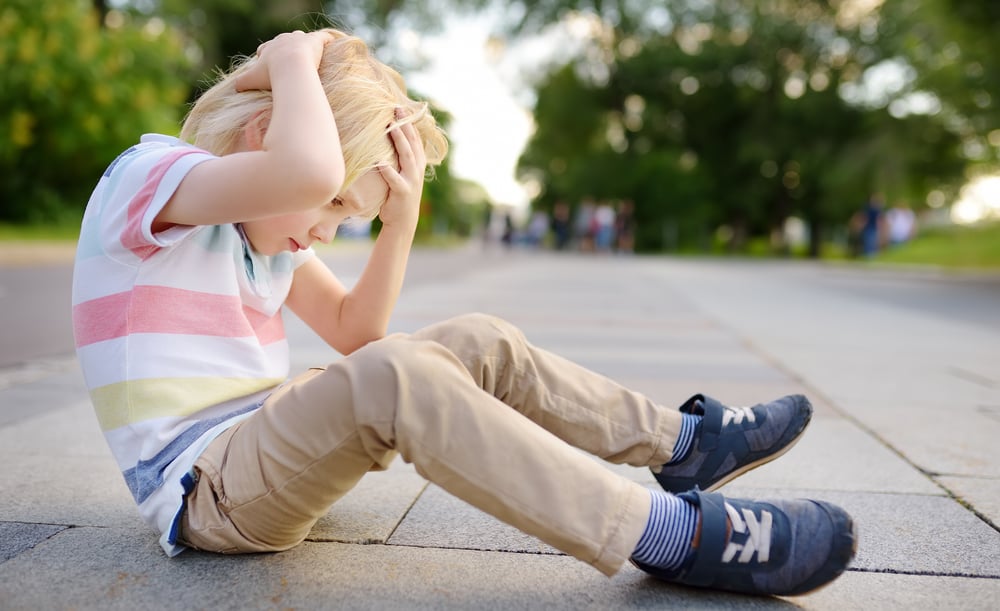 A little boy is sitting on the ground after hitting his head.