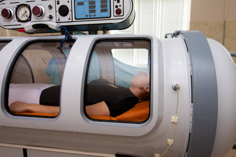 A woman lying in a machine receiving hyperbaric oxygen treatment.