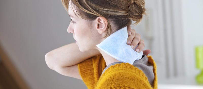 A woman holding a heating patch on her neck.