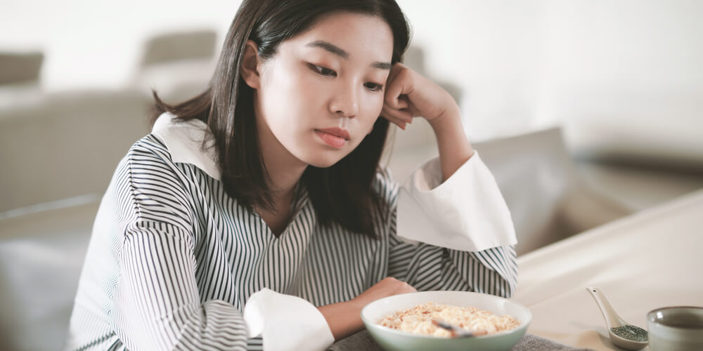 A woman is sitting down at the kitchen counter looking at a bowl of food.