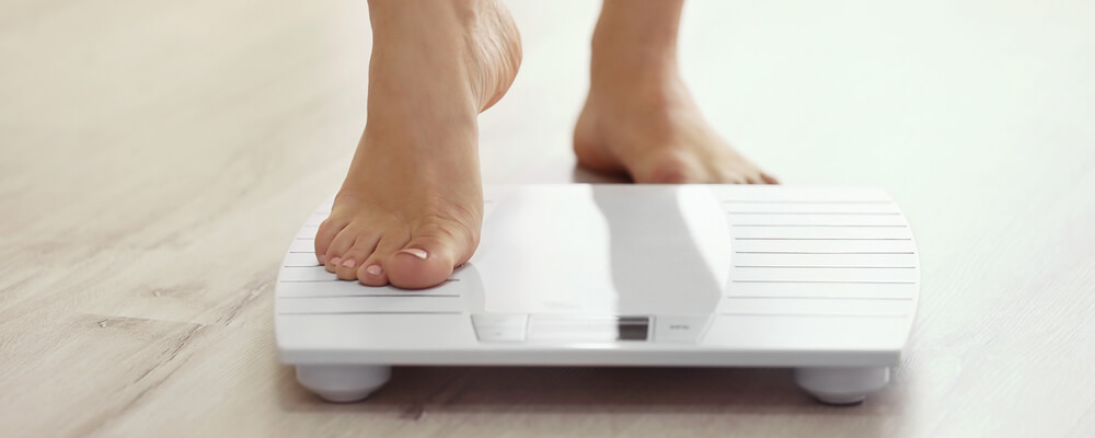 A woman is stepping on a scale in the bathroom.