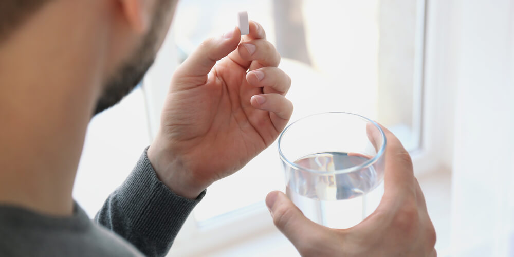 A man is holding a vitamin in one hand and a glass of water in the other hand.