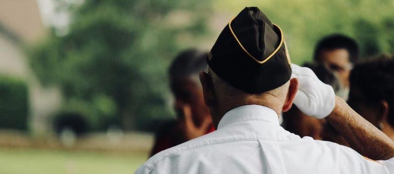 A photo of a veteran from behind wearing his hat while saluting.