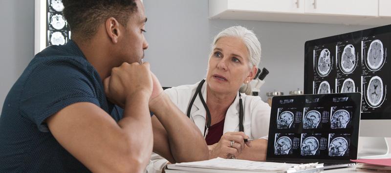 A female doctor is speaking with a young adult male client while looking over brain scans.