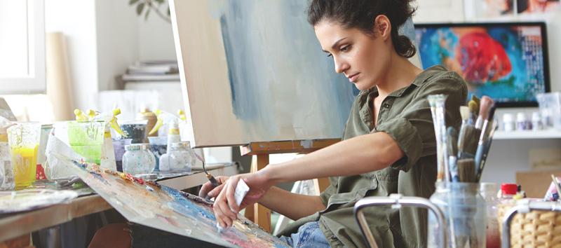 A young woman and artist is sitting down in a chair adding paint to her palate.