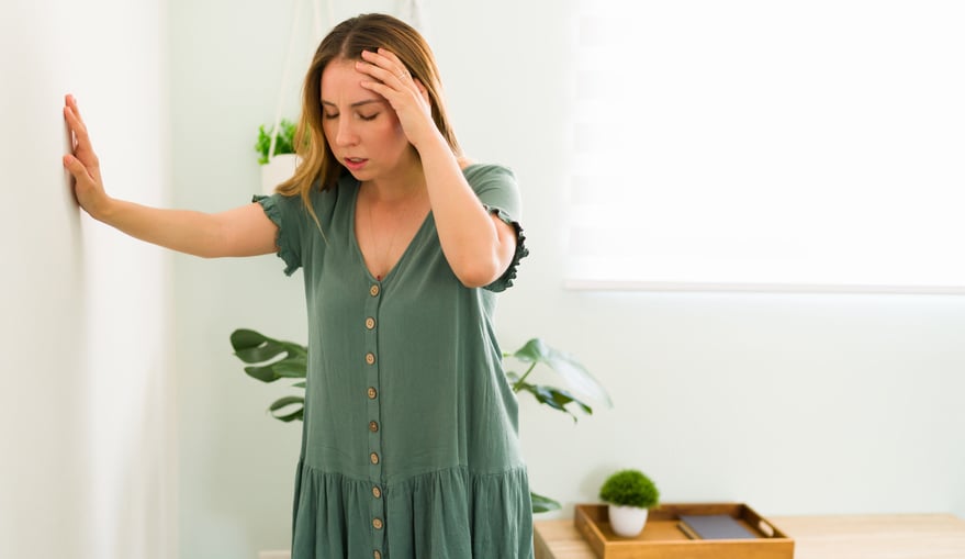 A woman leans into the wall while grabbing her head.