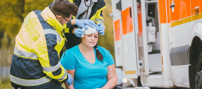 A women I sitting next to an ambulance while a few medics look at her.