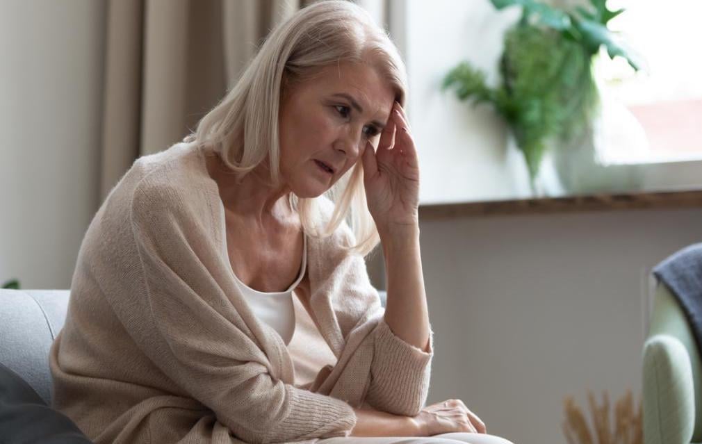 A woman is sitting on a couch and holding her forehead with her hand.