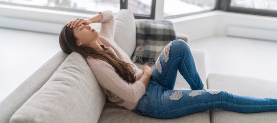 Image of woman sitting on couch holding her head in discomfort.