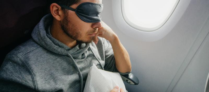 A man resting on the plane with an eye mask covering his eyes.