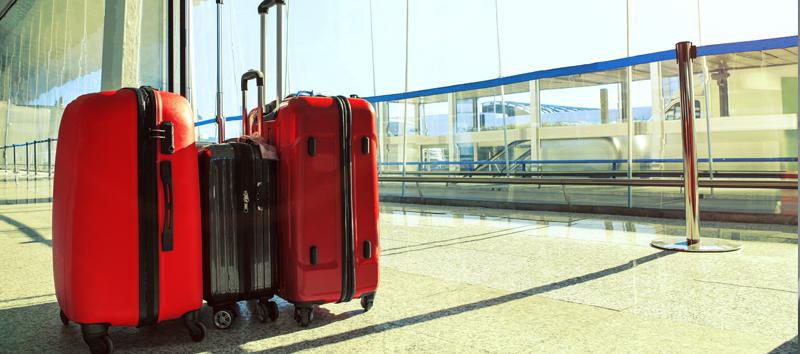 A photo with 3 rolling luggage bags (2 red and 1 black) at the airport.