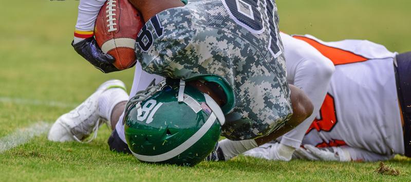 2 teams playing football and one player is falling to the ground and hitting his head while holding the football in his arm