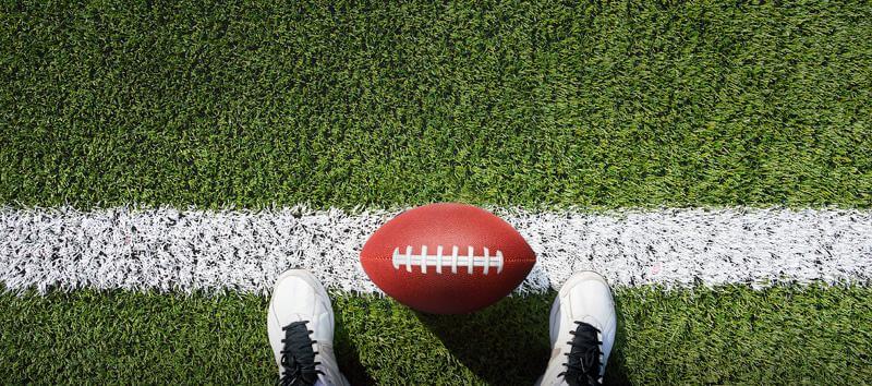 A picture of someone looking down at their feet on the sidelines with a football.