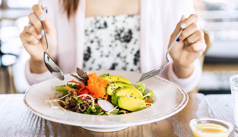 A woman is sitting eating a fresh salad for lunch.