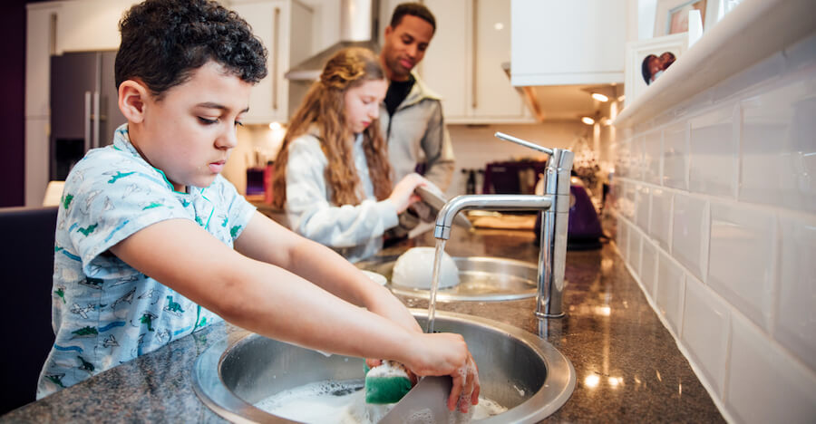 A dad is cleaning up the kitchen with his two kids washing the dishes