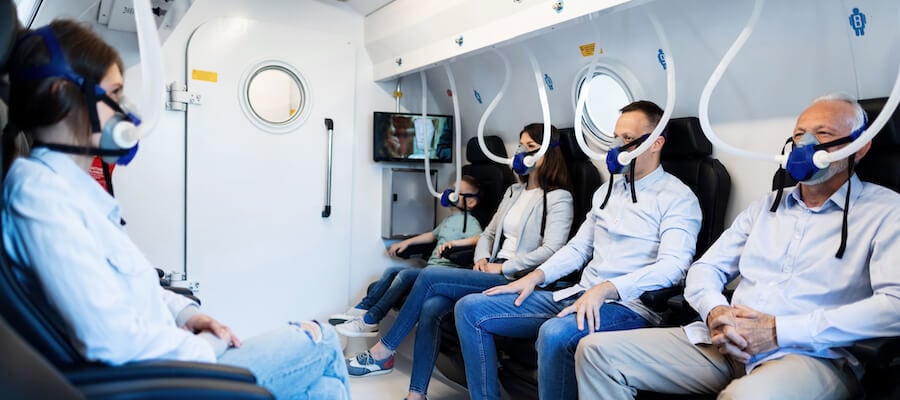 Patients getting HBOT shown sitting down in a hyperbaric chamber with oxygen masks.