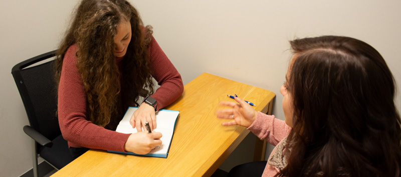 image of a woman helping a younger woman work through feelings by writing them down and talking about it