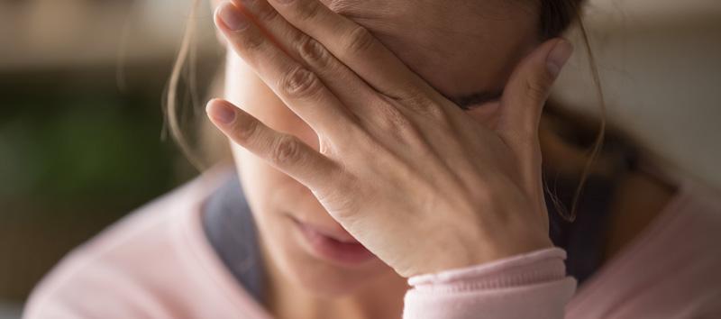 A woman sitting down and covering her eyes with her hand. 