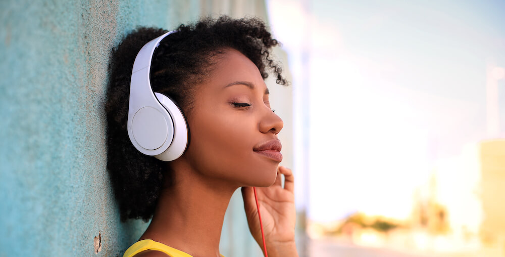 A woman wearing headphones leans against a wall while listening to her music.