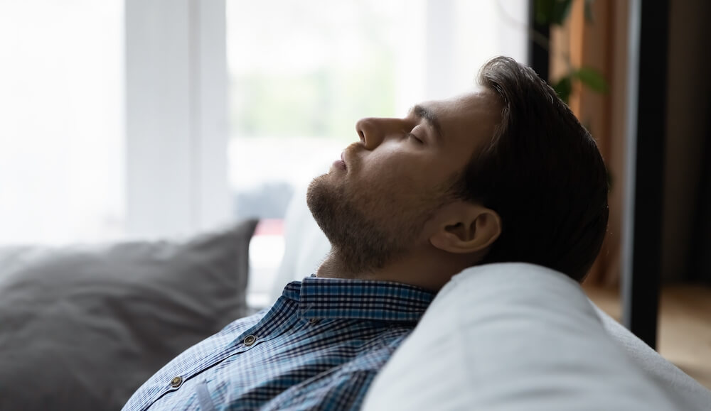 A man is lying his head back on the couch trying to relax after a stressful day