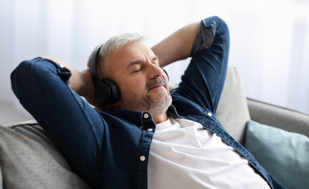 A man is relaxing by listening to music and reclining back on his couch
