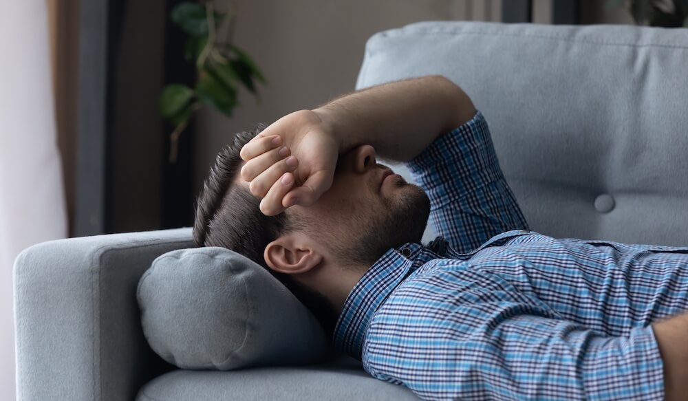 Man lying down on couch while grabbing his head.