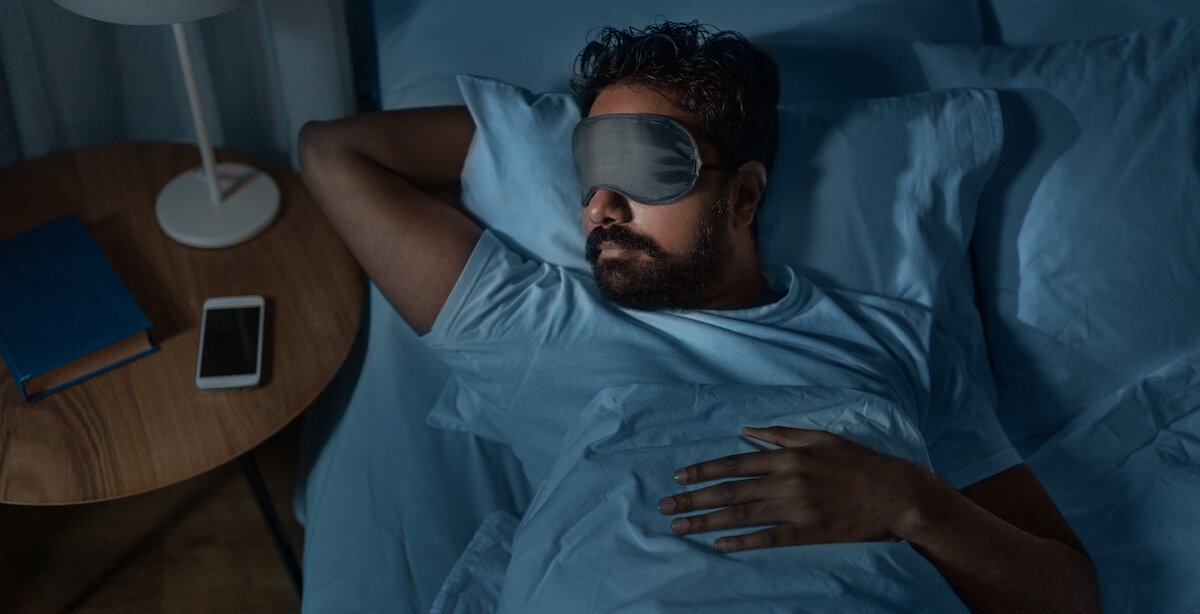 Man sleeping in bed with a sleep mask
