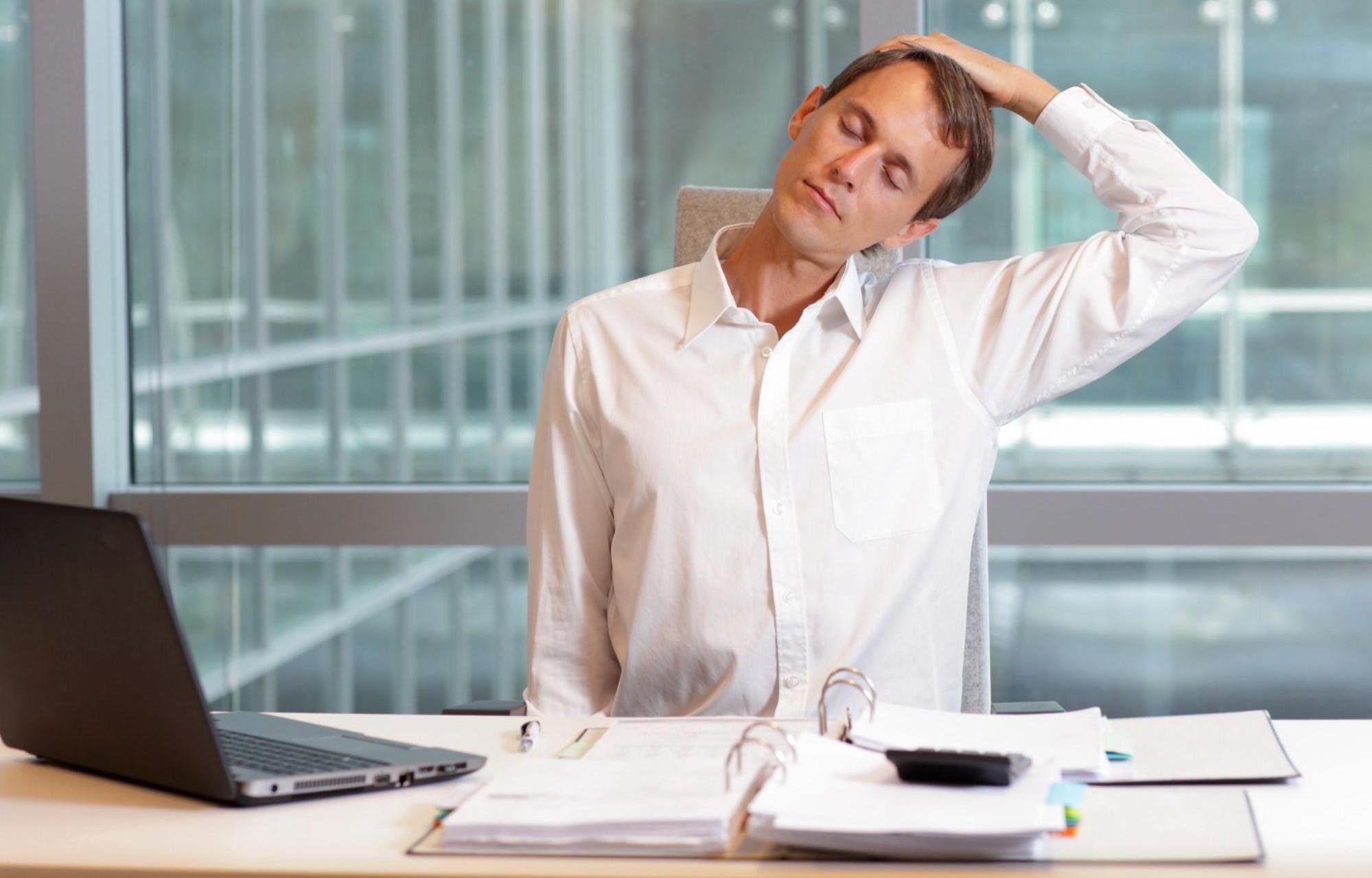 A man is stretching his neck at his desk in his office