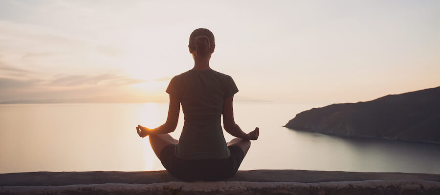 A woman is meditating while overlooking the ocean.