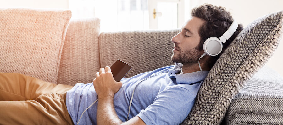 A man is relaxing on the couch with headphones in and his eyes closed.