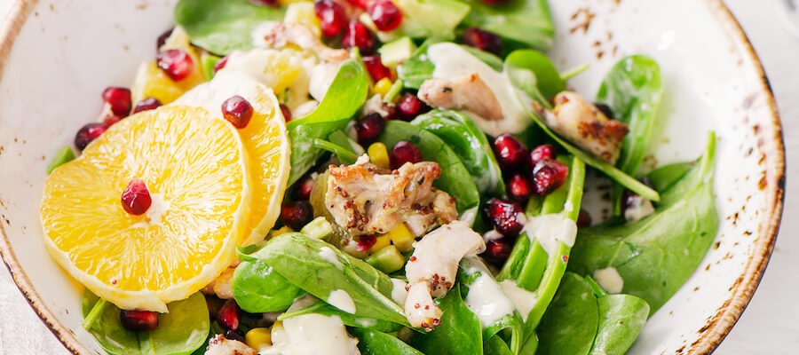 A photo of a fresh bowl of salad with pomegranate seeds, quinoa, orange slices, and chicken breast, served over spinach.