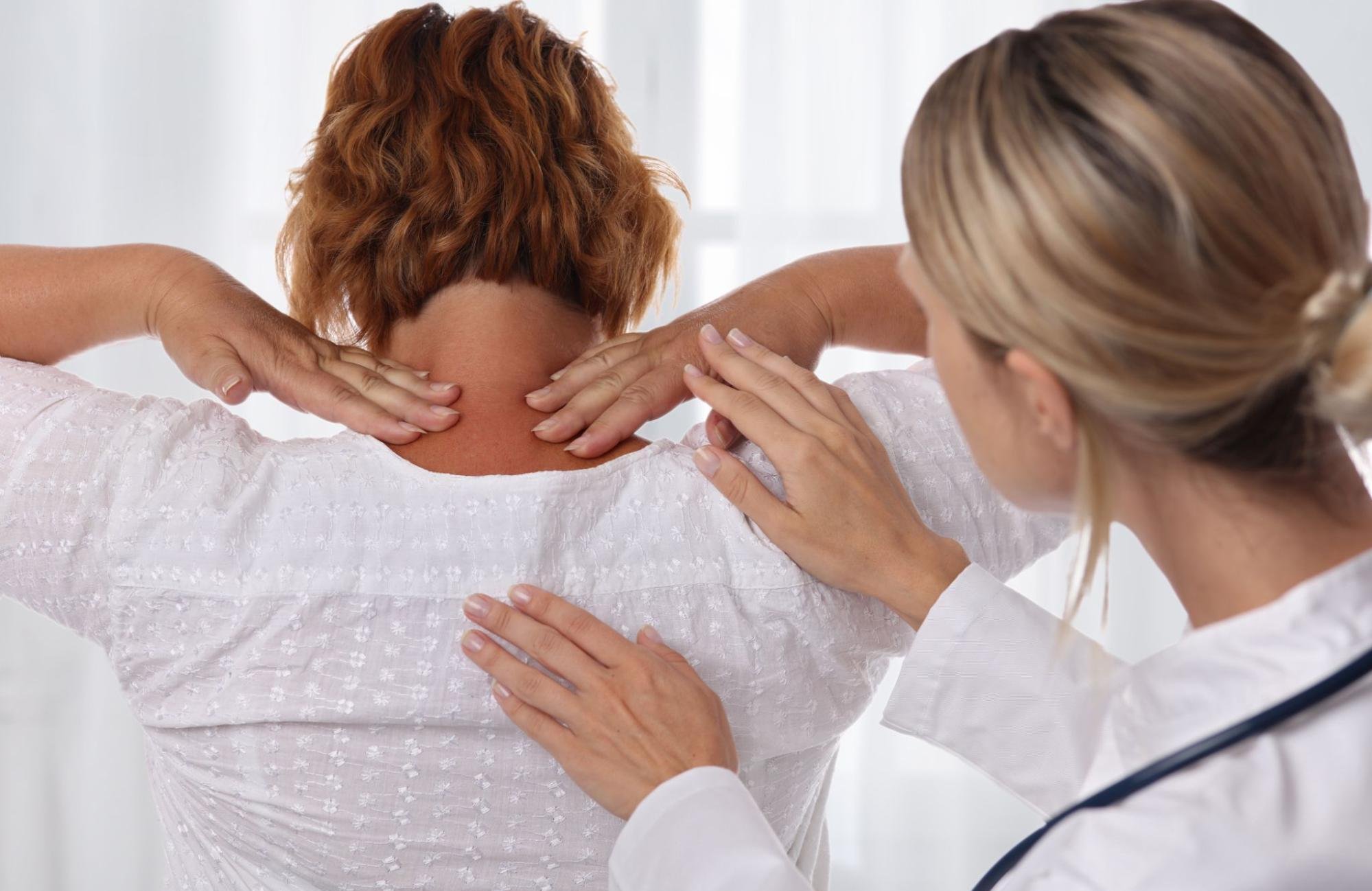 A patient is holding her neck while her doctor runs some tests