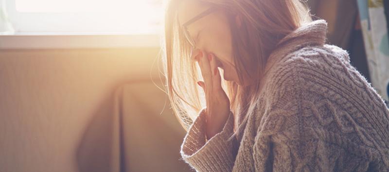 A young woman with glasses is covering her mouth while she yawns.