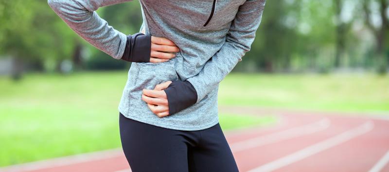 A woman grabs her side after her exercise has left her feeling under the weather.