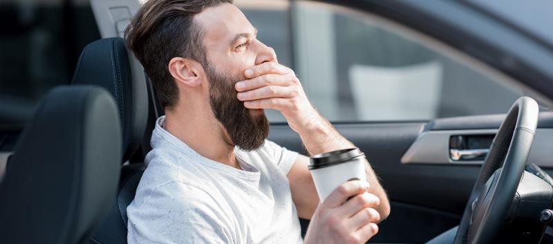 A man is parked in his car with a cup of coffee.