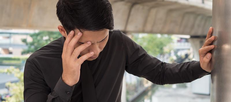 A young man grabs his forehead while leaning into a structure.