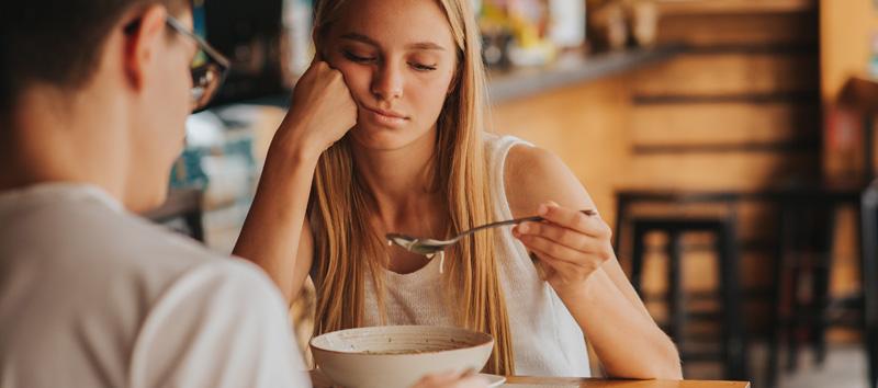 A young woman is sitting at a table staring down at her spoon.