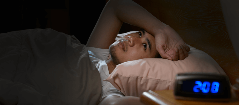 A young man is lying in bed during the middle of the night at 2am. 