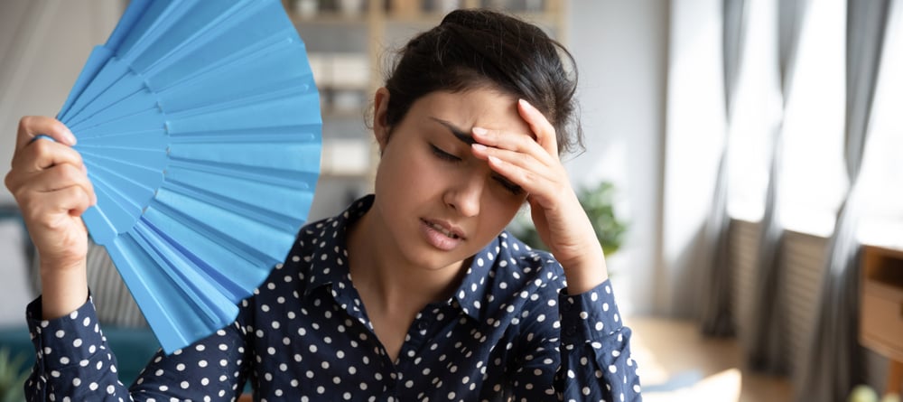 A woman is fanning herself while holding her head.