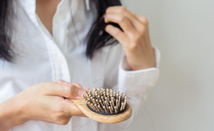 A woman holds her hairbrush with hair.
