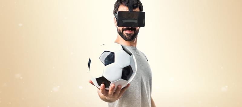 A man holding a soccer ball and wearing virtual reality headgear.