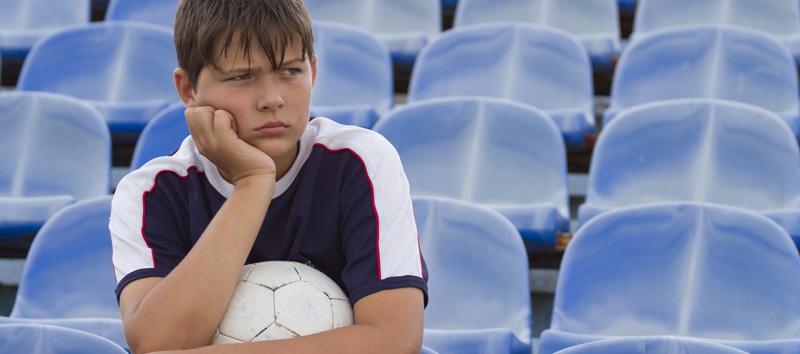 A young boy is sitting on the bleachers holding a soccer ball with his hand on his chin.