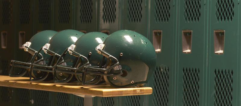 4 green football helmets in front of lockers in a locker room.