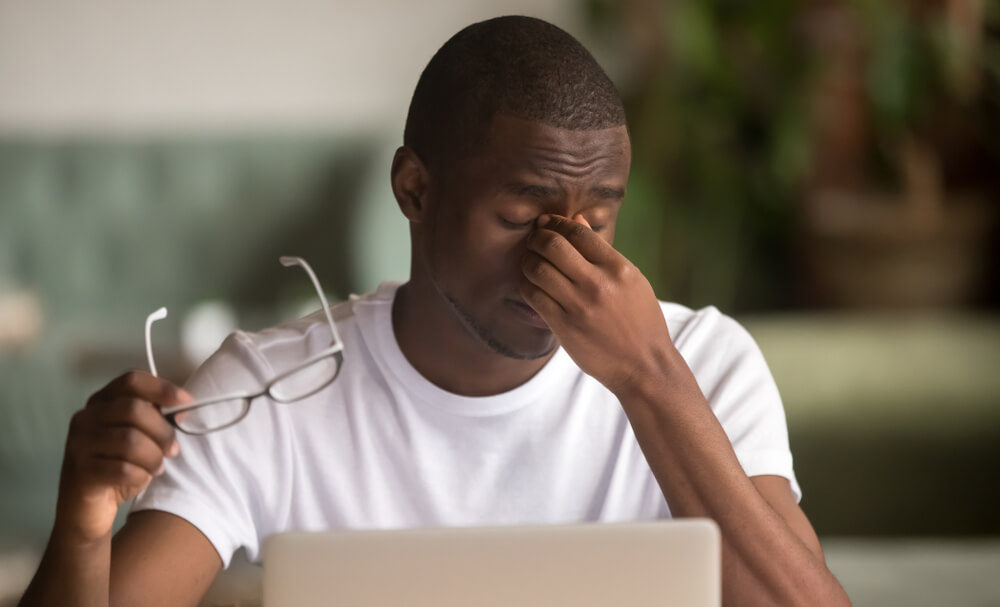 A stressed out man grabbing the root of his nose while working